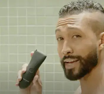 man holding body hair trimmer in shower